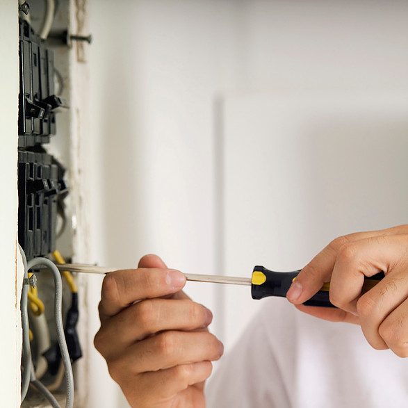 Electrician using a screwdriver to work on electrical wiring inside a panel.