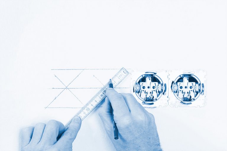 Person drawing electrical plans with a ruler next to two power sockets.