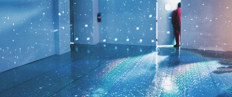 Person standing in a blue room filled with scattered light reflections and sparkles